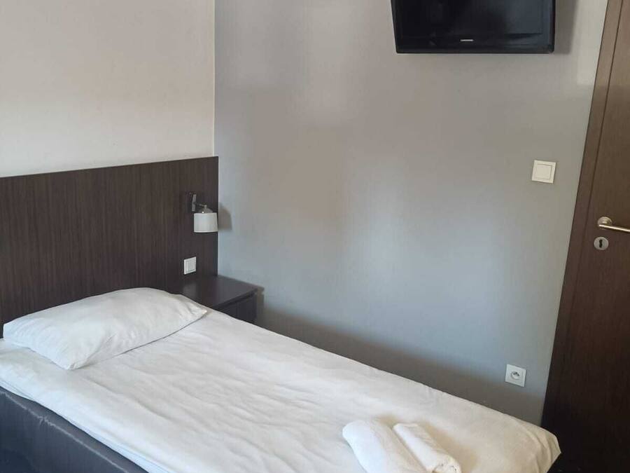 Une chambre d’hôtel avec un lit simple, un téléviseur à écran plat fixé au mur, une table de chevet et une porte.