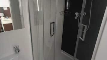 Un baño moderno con ducha de vidrio, un lavabo blanco y un espejo.