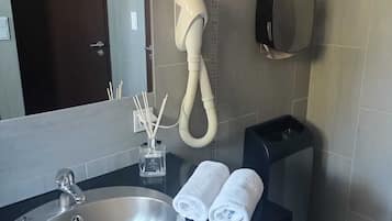 Un baño moderno con un lavamanos grande, un secador de pelo, un dispensador de toallas y un espejo.