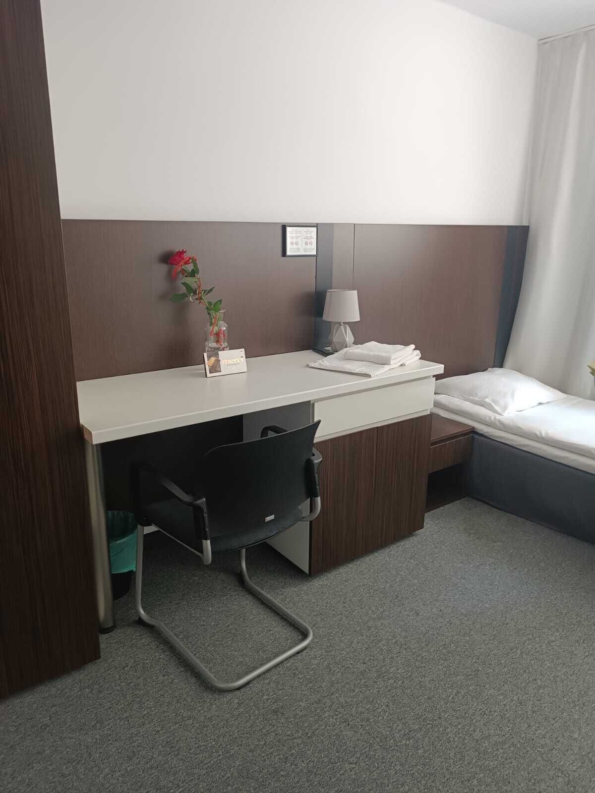 Een hotelkamer met een bureau, stoel, bed en een klein nachtkastje met lamp.