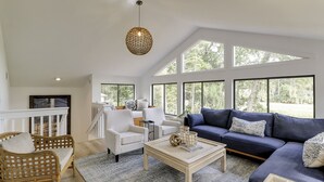 Un salon spacieux avec un plafond haut, de grandes fenêtres et un mélange de meubles, notamment un canapé, des fauteuils et une table basse.