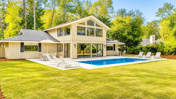 Une maison à deux étages dotée d’une piscine, d’un espace extérieur aménagé et d’une grande porte d’entrée en verre.