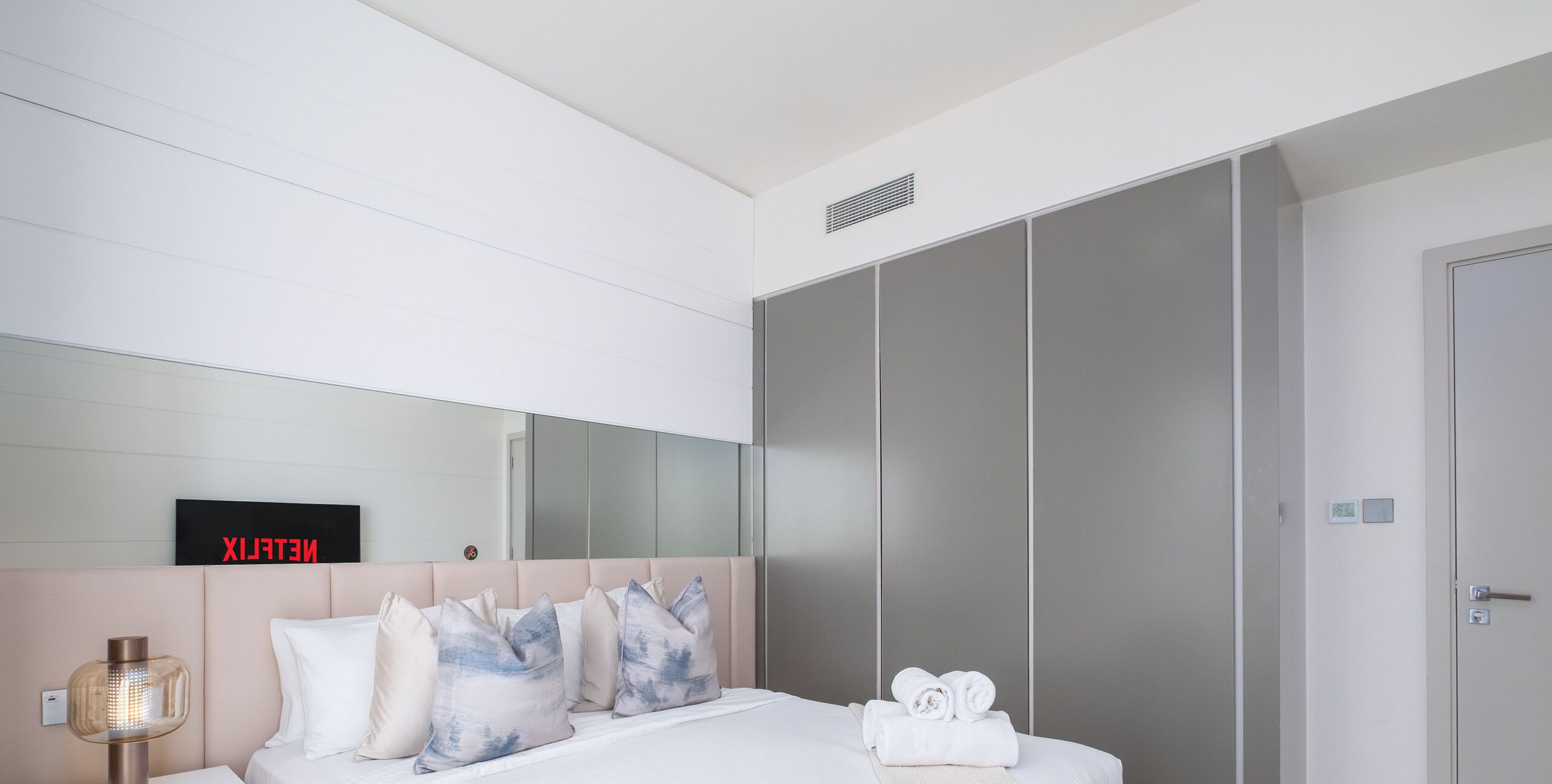Une chambre d’hôtel moderne équipée d’un lit, d’une table de chevet, d’un miroir et d’une armoire.