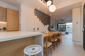 A modern kitchen with a central island, wooden chairs, and a white woven stool.
