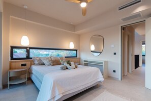 A bedroom with a large bed, bedside tables, a window with a view, a ceiling fan, and a mirror.