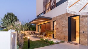 Una casa moderna con fachada de piedra, un patio con mobiliario exterior y una entrada bien iluminada.