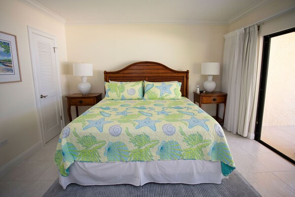 A bed with a starfish and coral pattern bedspread, two bedside lamps, a wooden headboard, and a view of the outdoors through a sliding door.