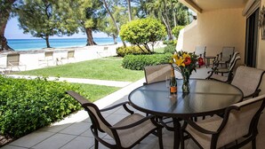 A patio with a round glass table and chairs, a vase with flowers, and a view of the ocean and trees.