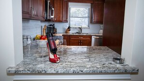 A kitchen with wooden cabinets, a granite countertop, a wine bottle, and a fruit bowl.