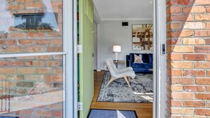 Ein Ziegelhaus mit grüner Tür, einem weißen Stuhl, einem blauen Sofa und einem Teppich im Innenraum.