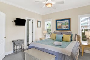 A bedroom with a bed, bedside tables, a desk, a ceiling fan, and a painting.