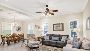 A spacious living room with a dining area, a ceiling fan, and a large window providing natural light. - Fully Upgraded Condo, Ideal for Families with Oasis Pool, Tiki Bar & Grill (Pensacola)