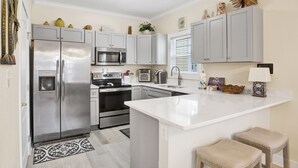A modern kitchen with stainless steel appliances, white cabinetry, and a central island. - Fully Upgraded Condo, Ideal for Families with Oasis Pool, Tiki Bar & Grill (Pensacola)