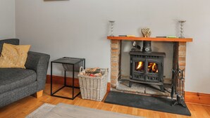 Una sala de estar con chimenea, un sofá, una cesta de mimbre con leña y un cuadro en la pared.