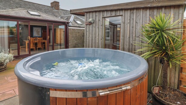 Un jacuzzi en un área exterior de madera con un patio y un edificio de madera al fondo.