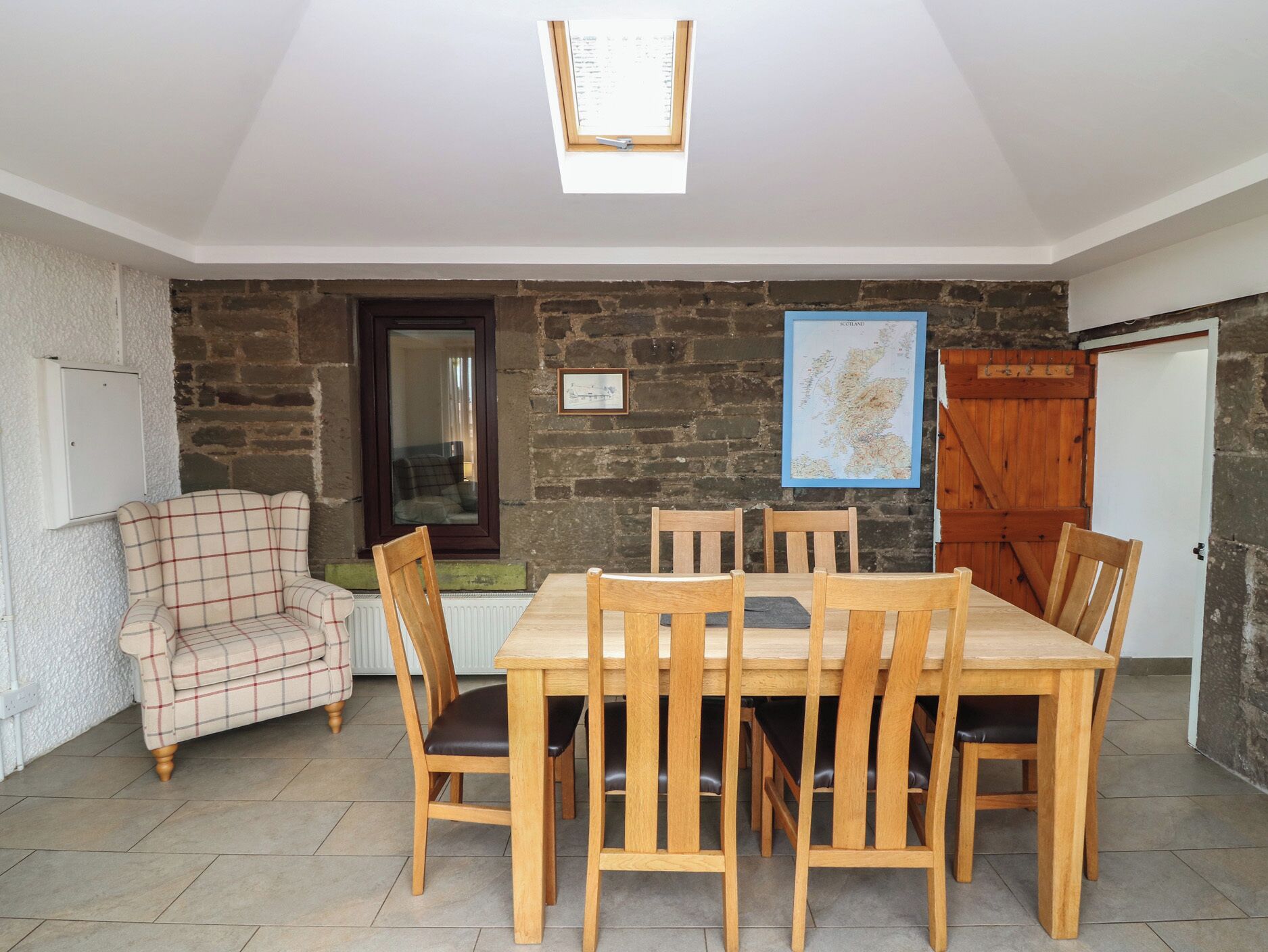A dining area with a stone wall, a map, and a plaid armchair.
