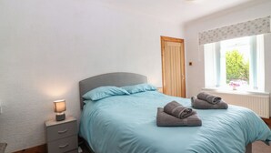 Un dormitorio con cama, mesita de noche, lámpara, ventana con vistas y puerta.