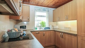 Una cocina con gabinetes de madera, microondas, pileta y ventana con vista a follaje.