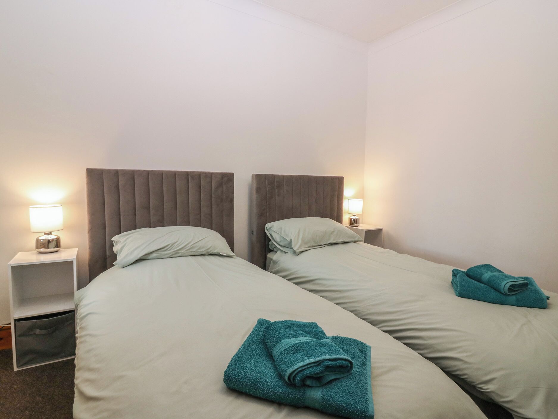 A hotel room with two beds, each with a headboard and bedside tables with lamps.