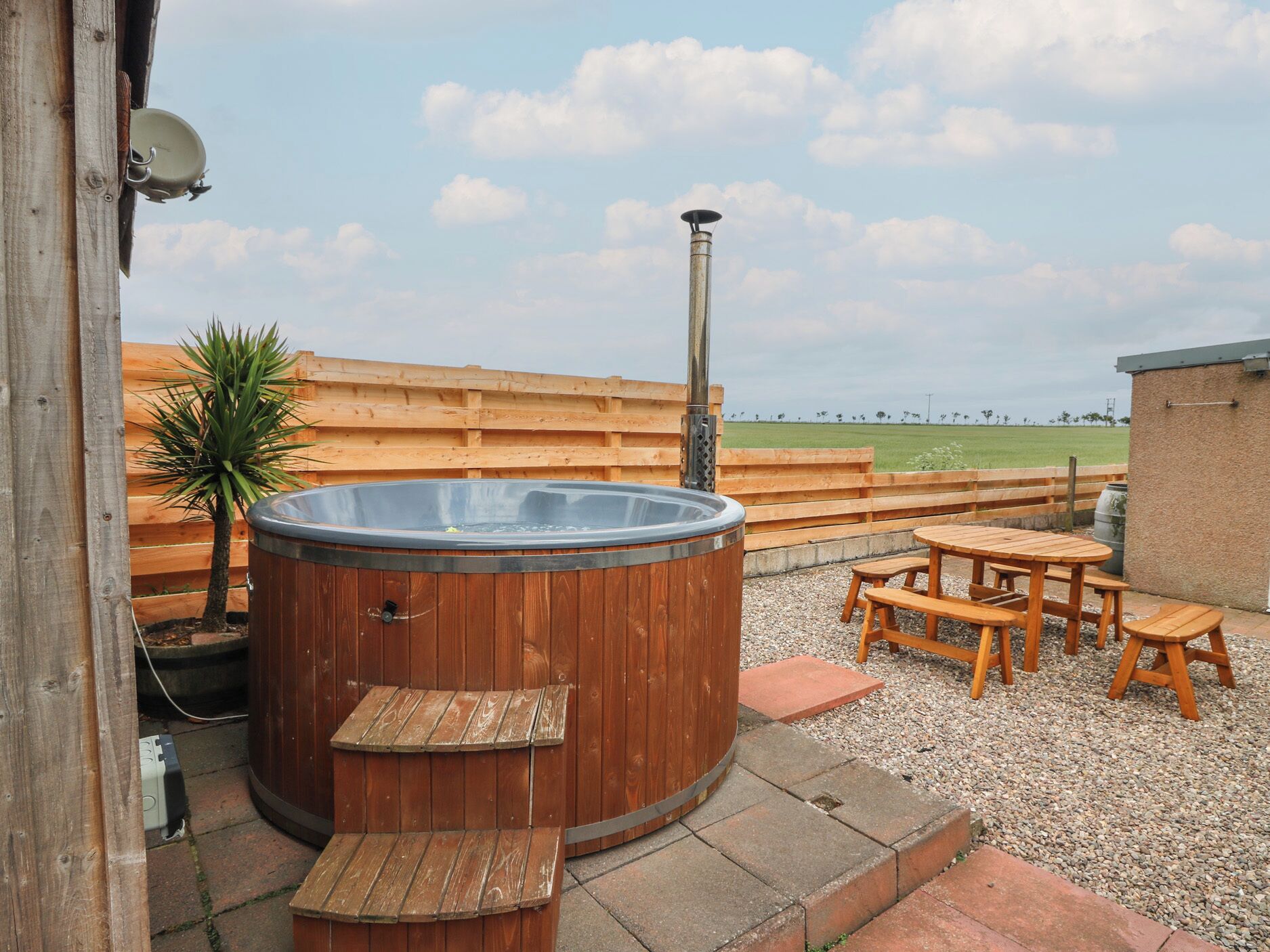 A hot tub with wooden benches, a wooden fence, and a grassy field in the background.
