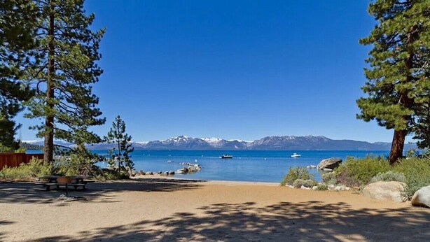 A clear view of a lake with mountains in the background, a picnic table, and a bench.