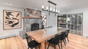 A spacious dining area with a large wooden table and black chairs, a stone fireplace, and artwork on the walls.