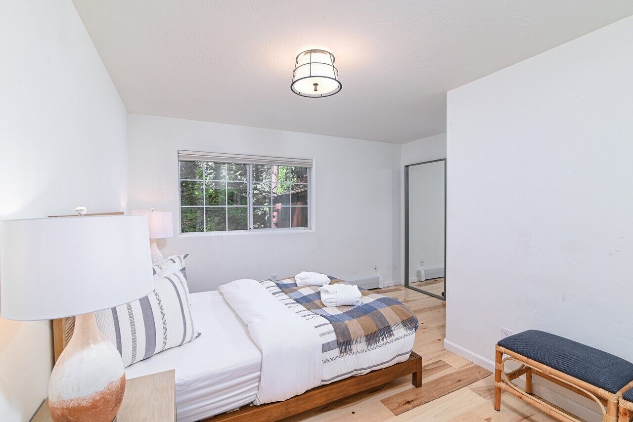 A bedroom with a bed, a bedside table with a lamp, a window, and a wooden bench.