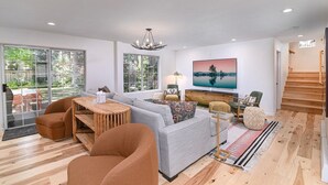 A modern living room with a sofa, armchairs, a wooden coffee table, and a TV.