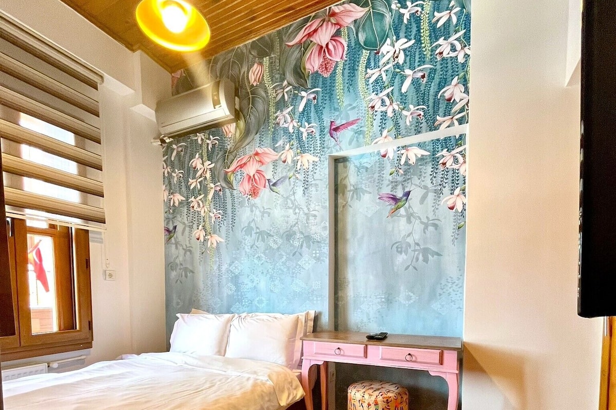 A bedroom with a bed, a desk, a chair, and a wall with floral wallpaper.