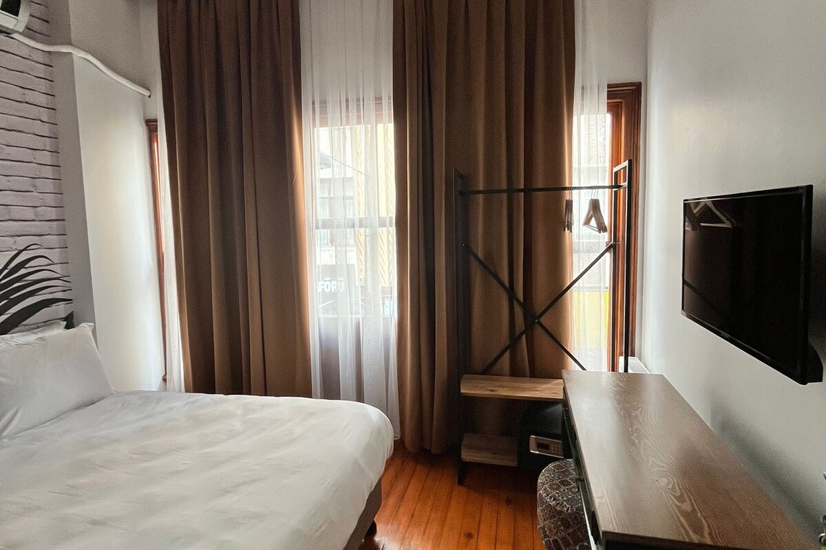 A hotel room with a bed, a desk, a TV, and a window with curtains.