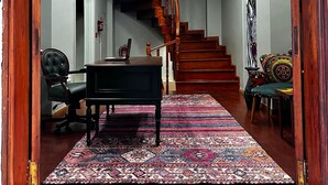 Un couloir avec un escalier en bois, un bureau avec une chaise et un tapis à motifs.
