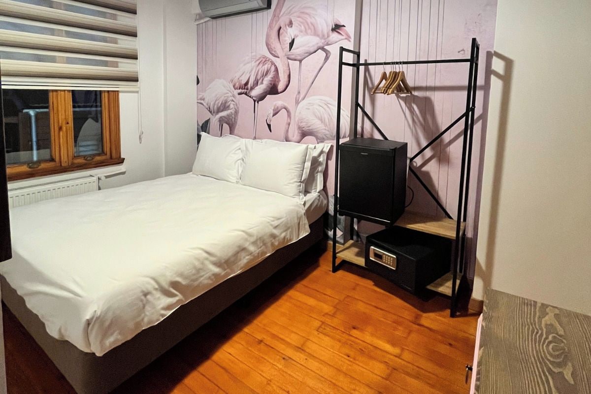 A bedroom with a bed, a wall-mounted TV, a wooden ceiling, and a window with blinds.
