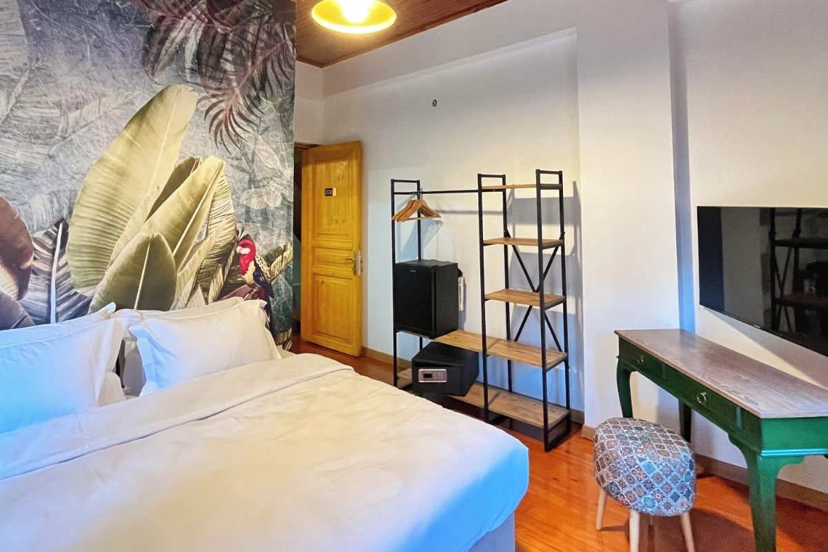 A bedroom with a bed, a desk, a chair, a TV, and a wooden ceiling.