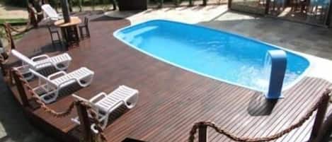 Una piscina al aire libre con sillones de descanso y una parrilla.