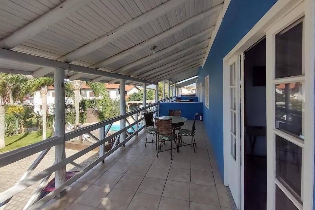 Un balcón techado con vista a la piscina, una mesa con sillas y una pared azul.