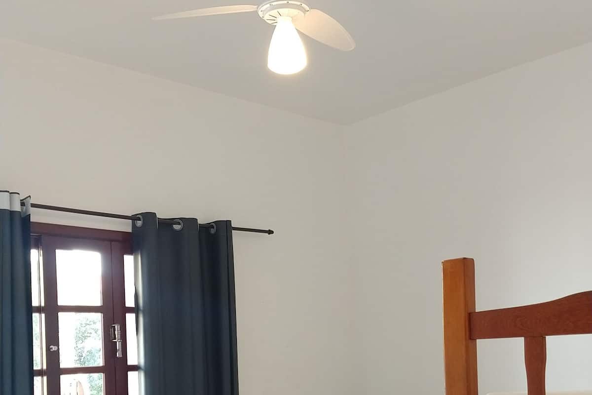 Habitación de hotel con una cama individual, una cama nido de madera, un ventilador de techo y una ventana con cortinas.