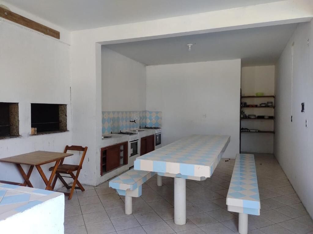 Een compacte keuken met een betegelde spatwand, een ingebouwde kookplaat en een klein spoelbakje. Er is een zithoek met een bank en een tafel, en een kleine houten stoel.