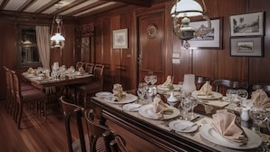A formal dining room with wooden paneling, a large dining table set for a meal, and hanging chandeliers. - Dahabeya Farouz El Nil I Nile Cruise (Luxor)