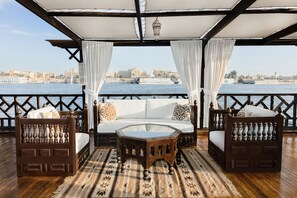 A balcony with a wooden floor, a glass-top coffee table, and two wooden chairs with cushions. - Dahabeya Farouz El Nil I Nile Cruise (Luxor)