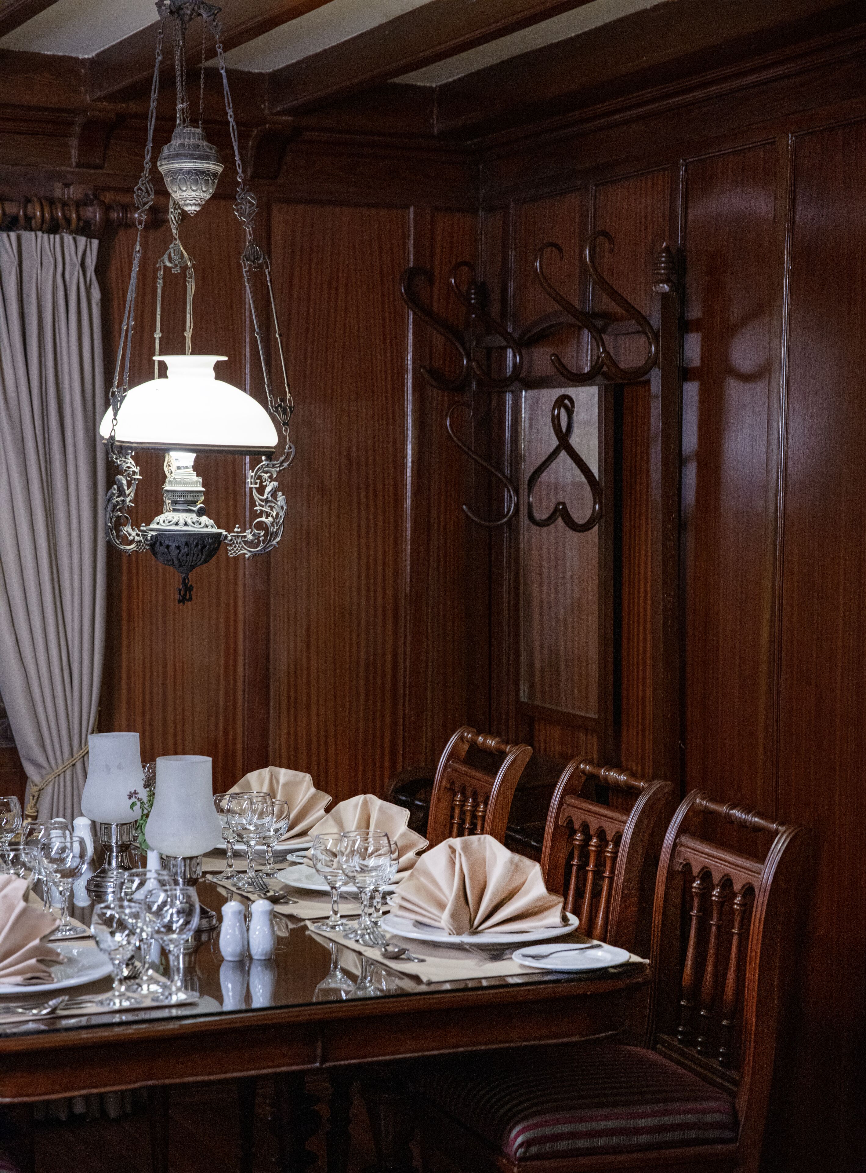 Une salle à manger formelle avec une table en bois dressée pour un repas, des chaises élégantes et un luminaire suspendu.