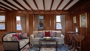A room with a sofa, armchair, and coffee table, wooden floors, and a large window with a view of the water. - Dahabeya Farouz El Nil II Nile Cruise (Luxor)