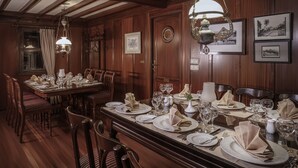 A formal dining room with wooden paneling, a large dining table set for a meal, and hanging chandeliers. - Dahabeya Farouz El Nil II Nile Cruise (Luxor)
