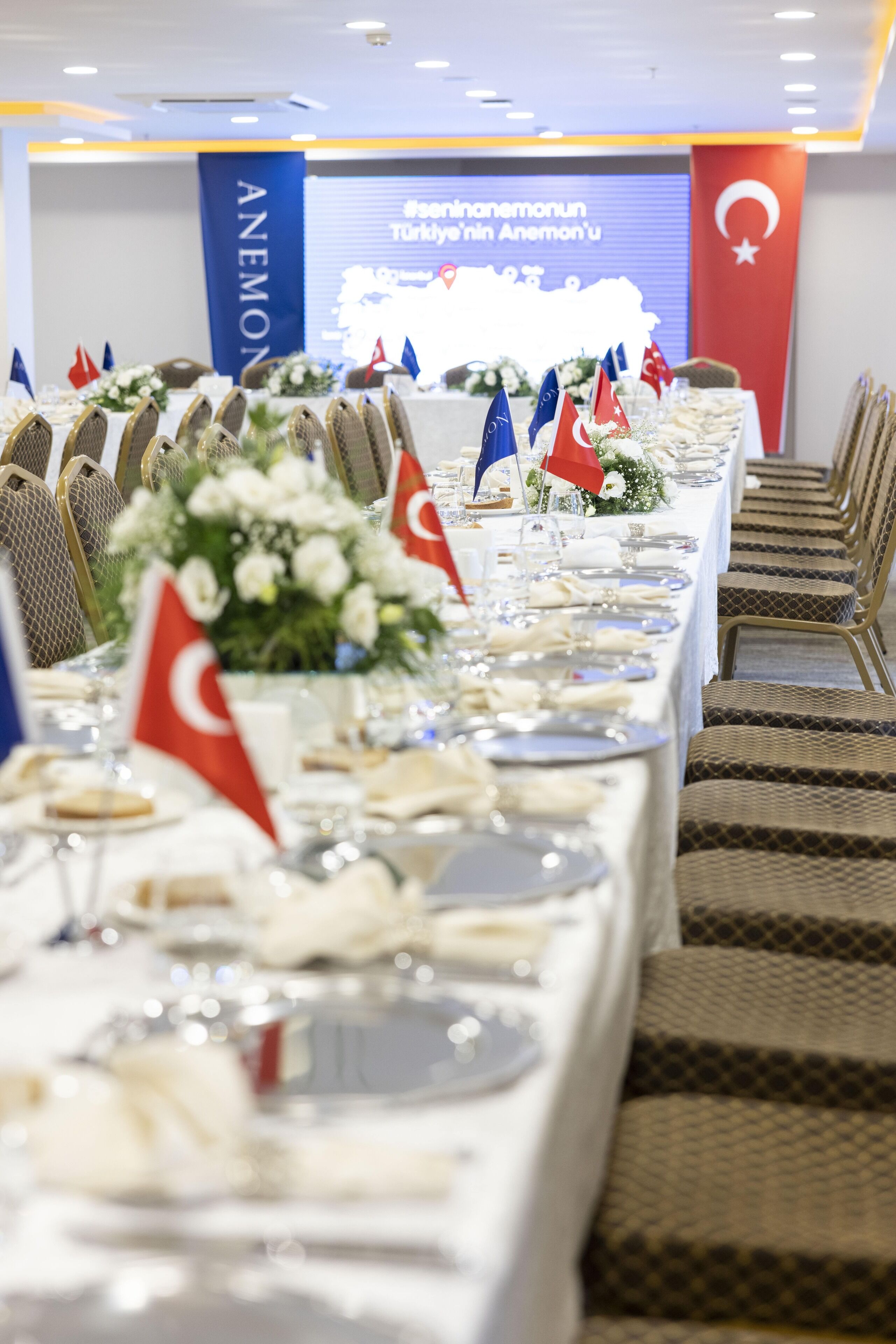 A conference room with a long table set for a meeting, flags of various countries, and a projection screen in the background.