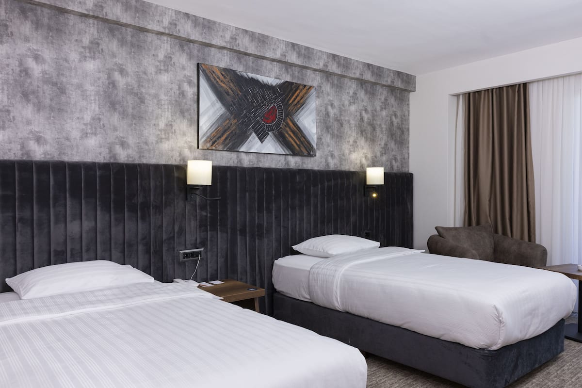A hotel room with two beds, a large abstract artwork on the wall, and a view of the outdoors.