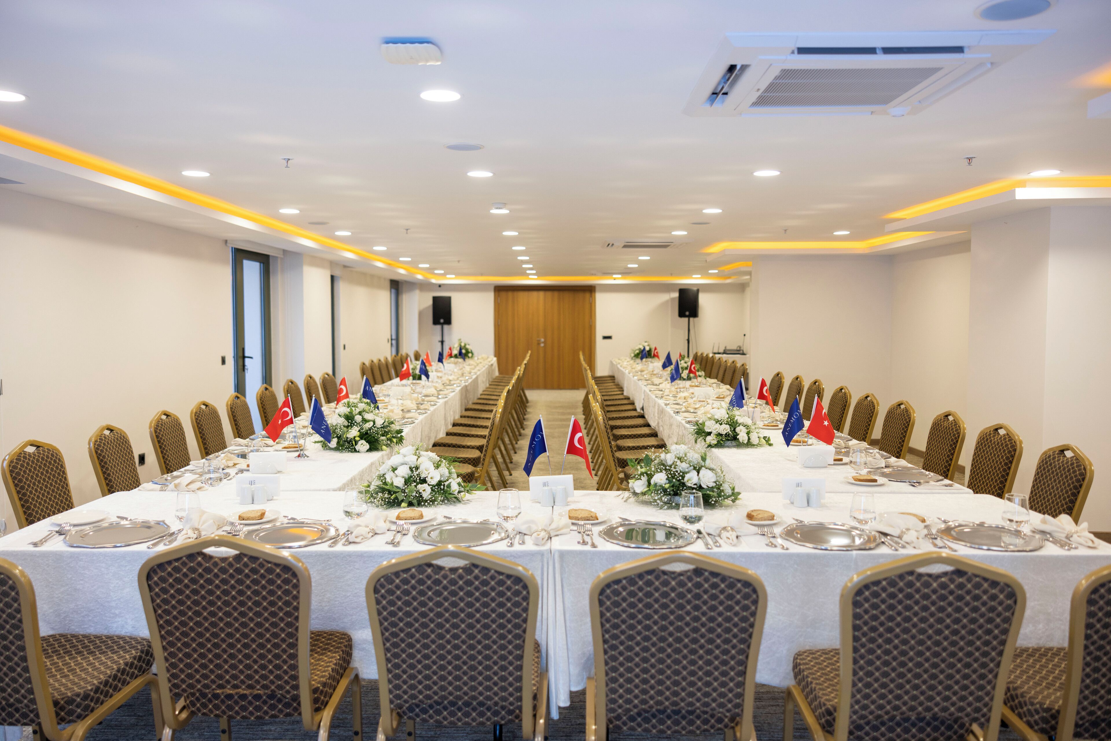 Un salón de conferencias con una larga mesa dispuesta para una reunión, flanqueada por filas de sillas y banderas de varios países.