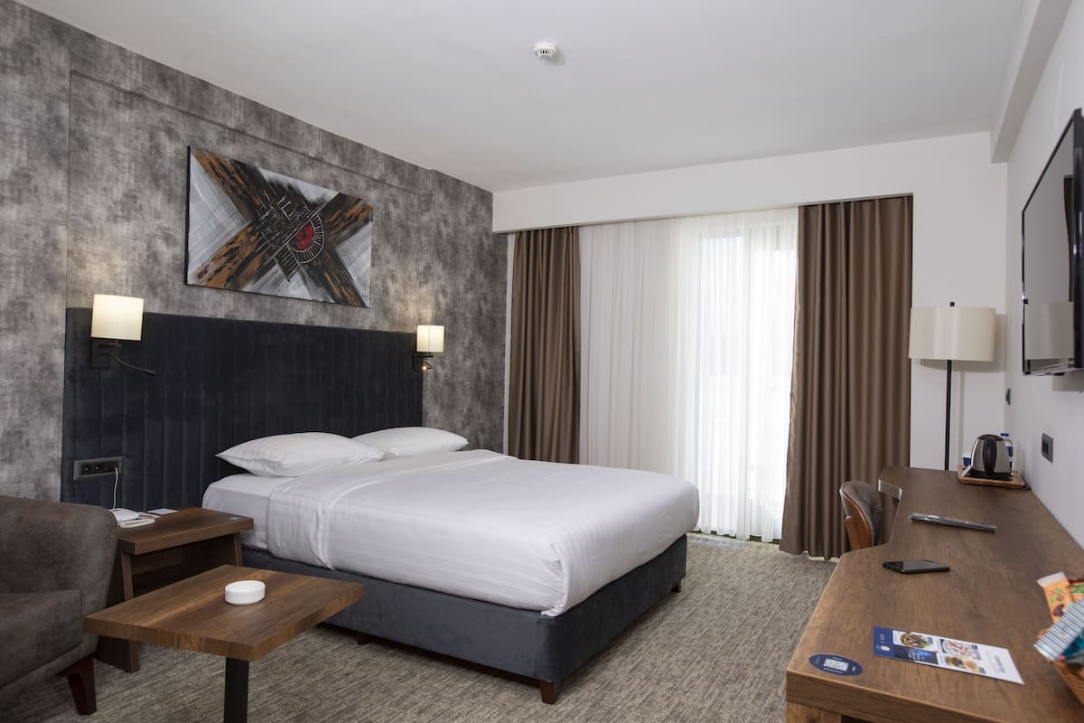 A hotel room with a large bed, a desk, a chair, and a TV.