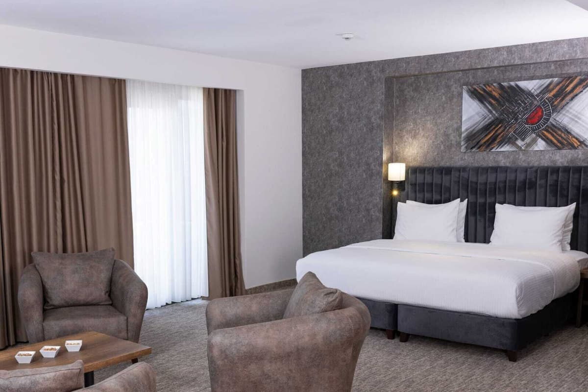 A hotel room with a large bed, two armchairs, a small table, and a wall-mounted artwork.