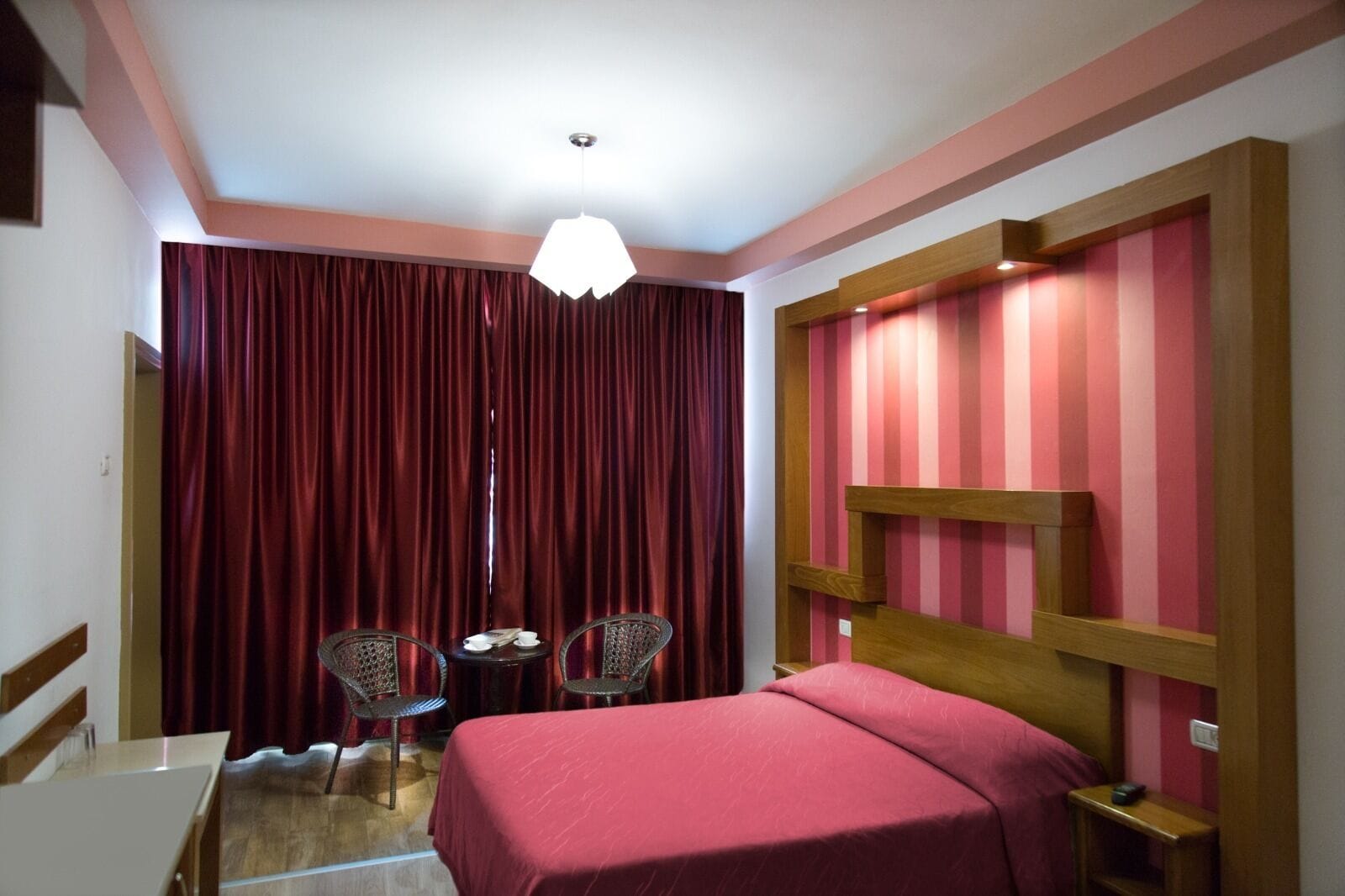 Een hotelkamer met een bed, een klein tafeltje met stoelen, een kroonluchter en een gestreepte wand.