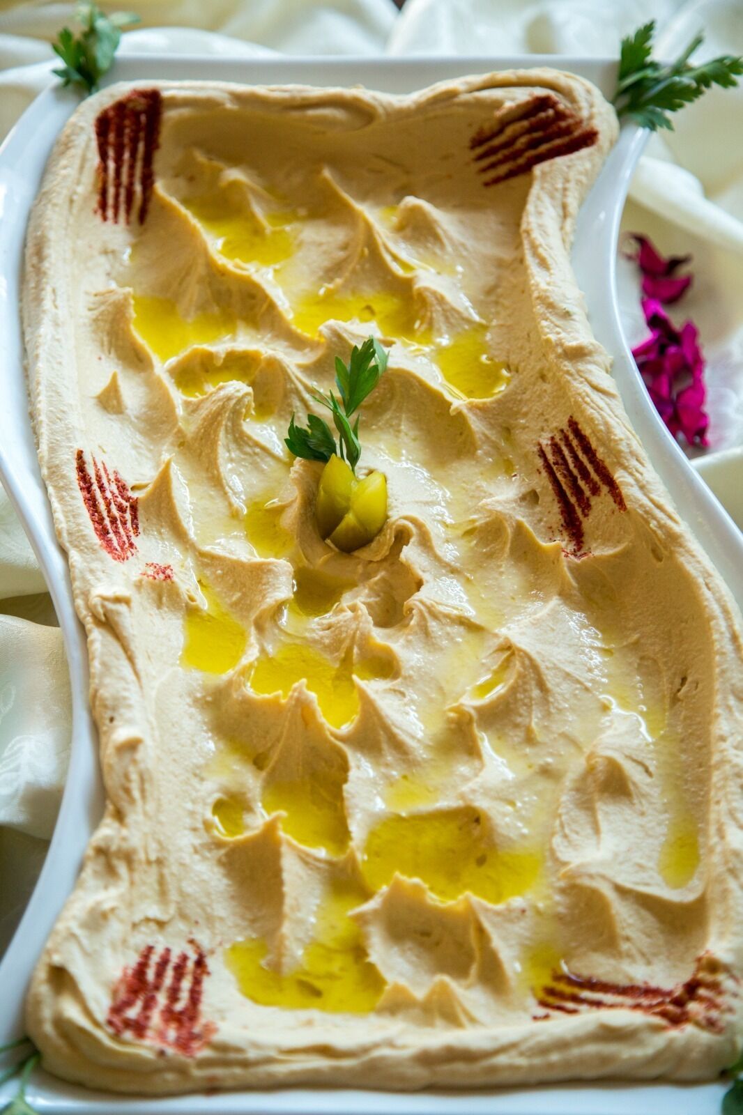 A rectangular white dish with a smooth, creamy substance, possibly hummus, garnished with olive oil and parsley.