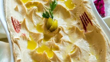 Un plato rectangular blanco con una sustancia cremosa y tersa, posiblemente hummus, adornado con aceite de oliva y perejil.